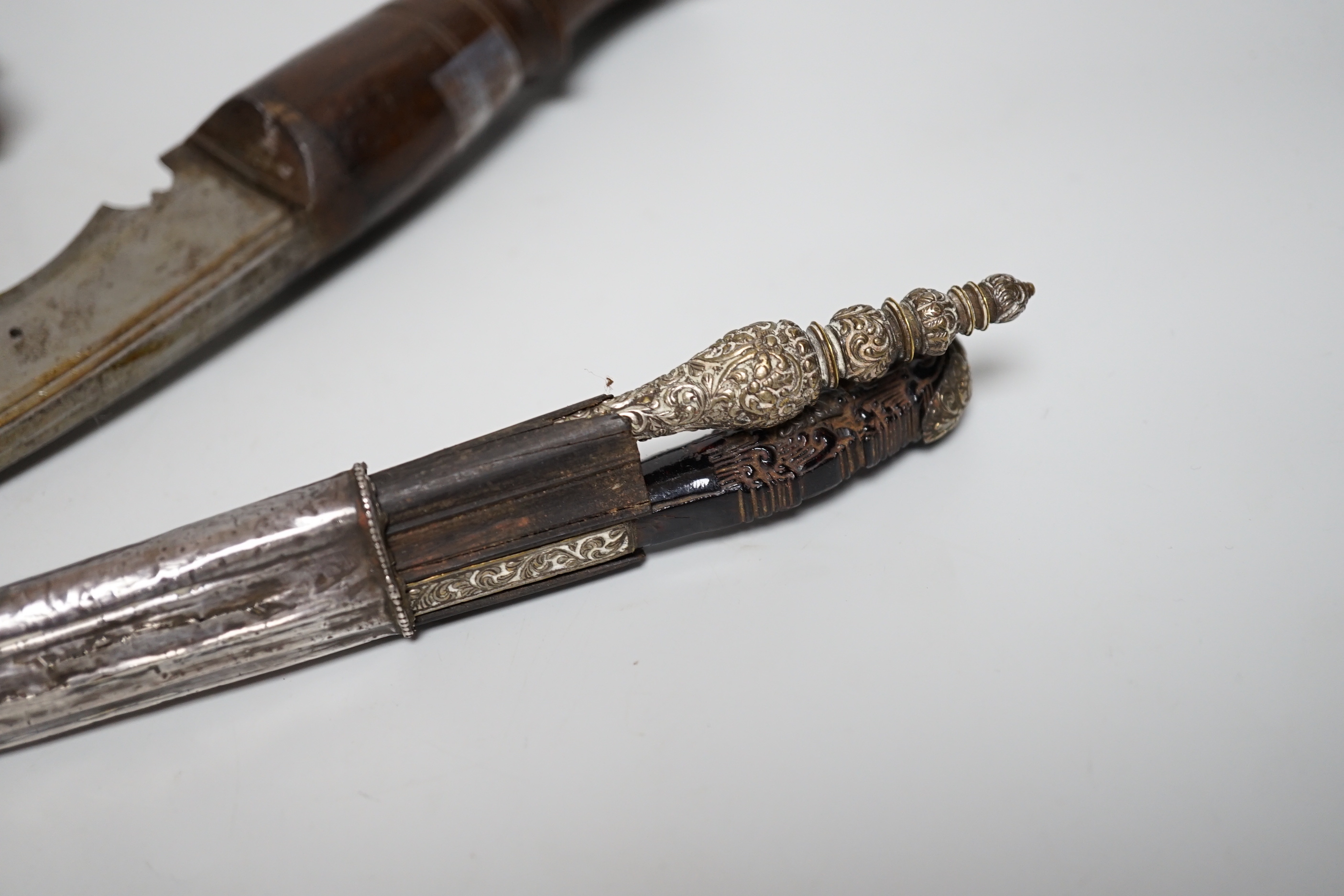 Two Sinhalese daggers and a kukri, a silver inlaid Kirichchiya dagger, together with another in a scabbard with a long pin, another dagger with a wooden handle, a head of a brass inlaid iron pole arm, a George V 1897 pat